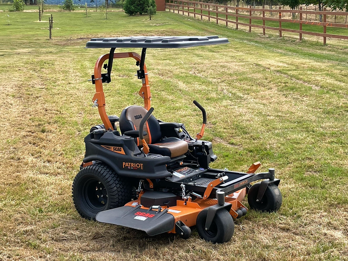A Patriot ZT200 zero-till riding lawn mower with an orange and black body, a black canopy roof, and a front deck guard, parked on a dry grassy field.